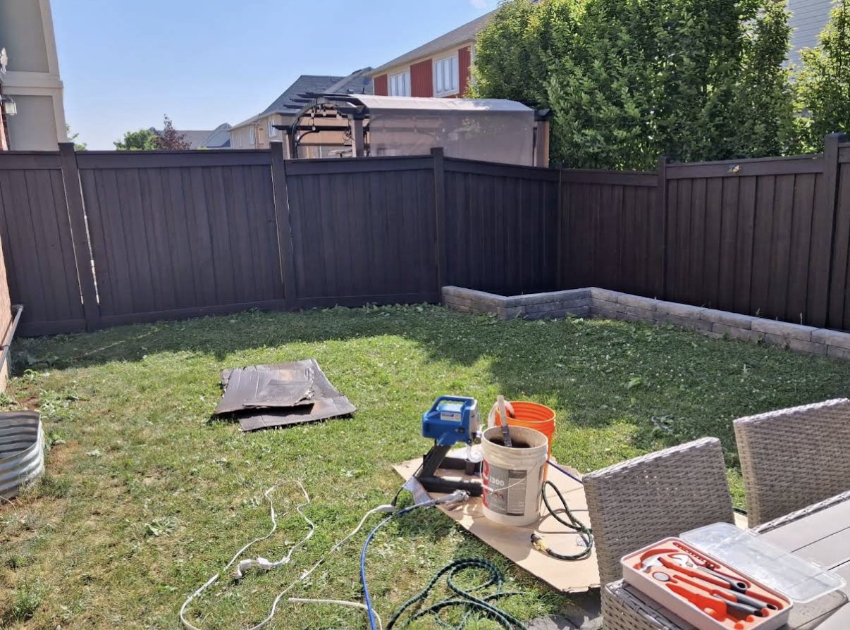 Backyard fence stained a deep espresso brown with the TrueCoat sprayer set up on the lawn